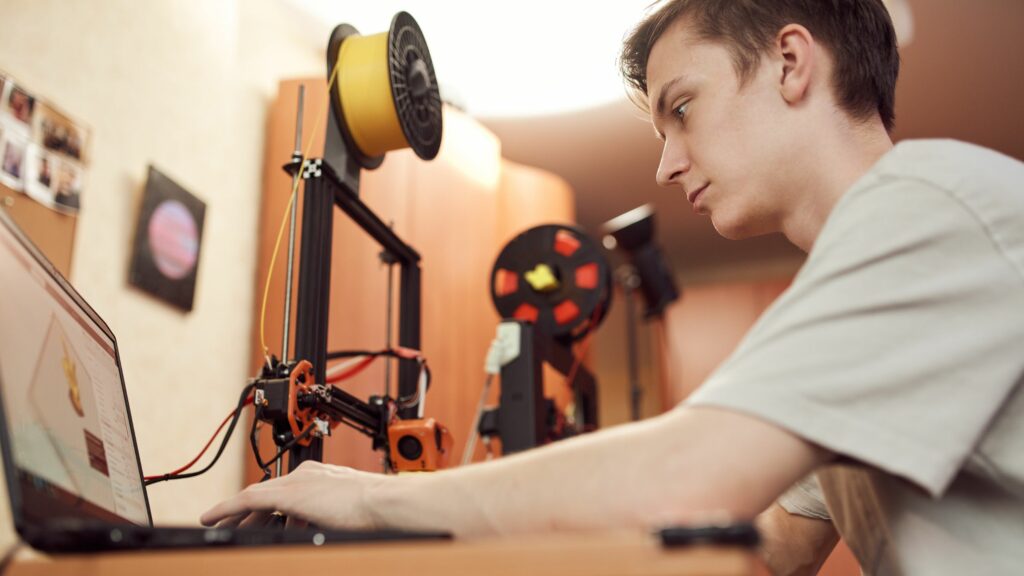 Mann sitzt hinter einem Labortisch und stellt einen 3D-Drucker ein