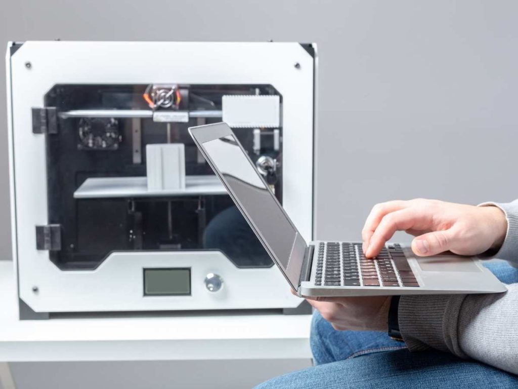 3d printer in the background with a laptop and a person typing
