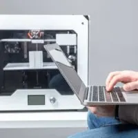 3d printer in the background with a laptop and a person typing