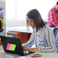 3d printer in the background with woman and laptop sending file to 3d printer
