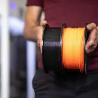 man holding two spools of filament in black and orange