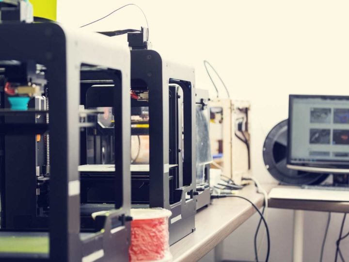 multiple 3d printers standing on a desk next to a labtop