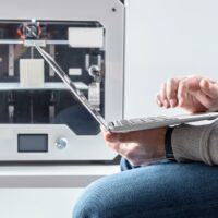 3d printer with enclosure and person using laptop