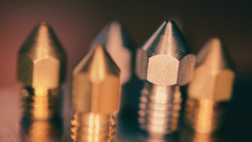 A close-up of four 3D printer nozzles with a focal nozzle marked '0.4'